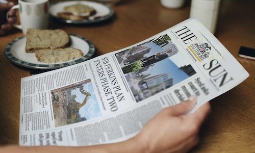 Person reading a newspaper cover story featuring the Perkins Plan entering Phase II